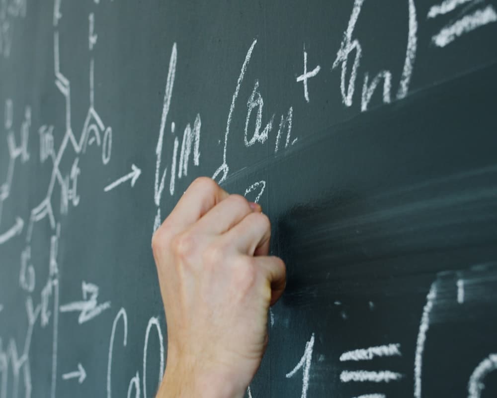 Kara tahtaya tebeşirle matematik formülü yazan bir öğretmenin eli